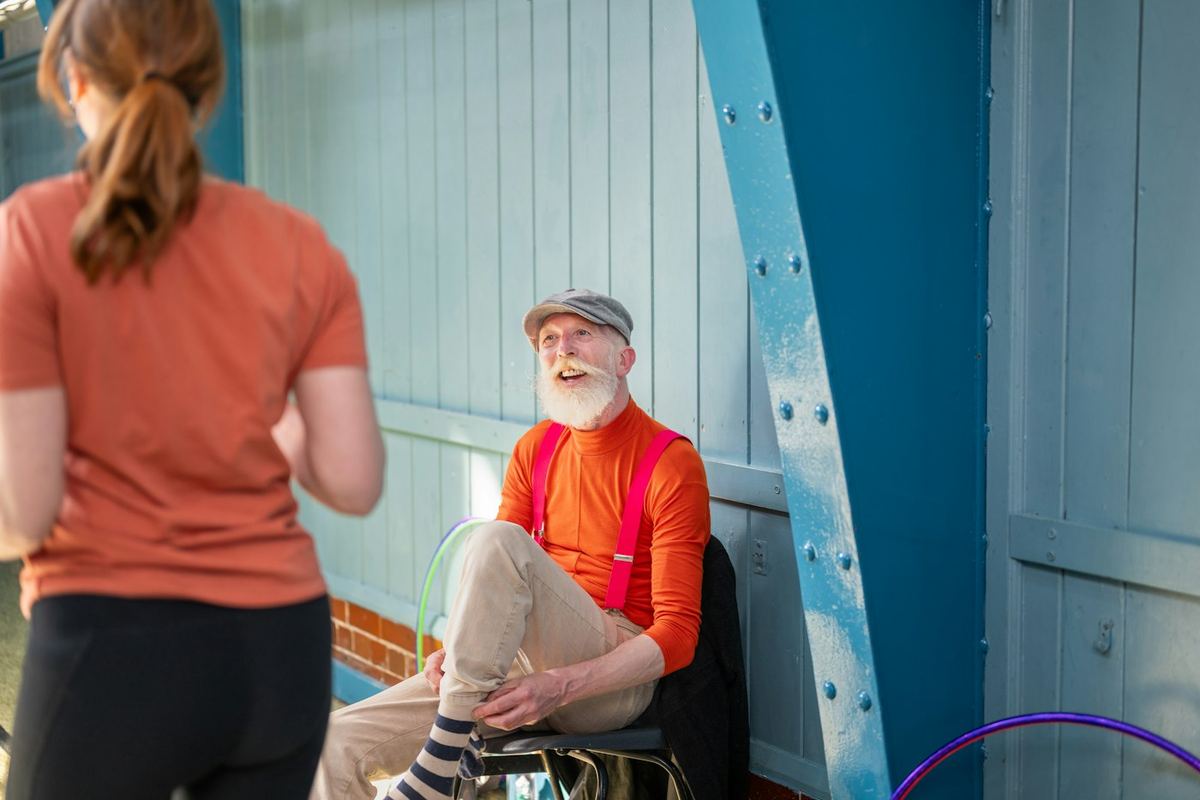 An older man in a hat and suspenders smiling
